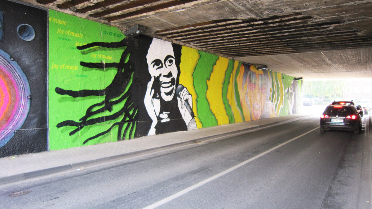 Streetart-Graffiti unter einer Brücke, das eine lächelnde Figur mit Mikrofon zeigt, umgeben v