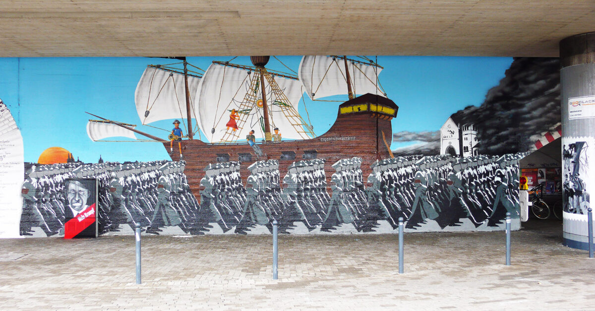 Wandgemälde in einem urbanen Raum, das ein historisches Segelschiff mit mehreren Figuren an Deck zeigt. Im Vordergrund sind marschierende Figuren zu sehen, während im Hint